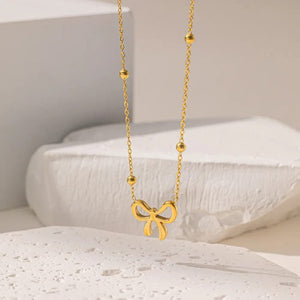 Gold bow pendant necklace with beaded chain on white background