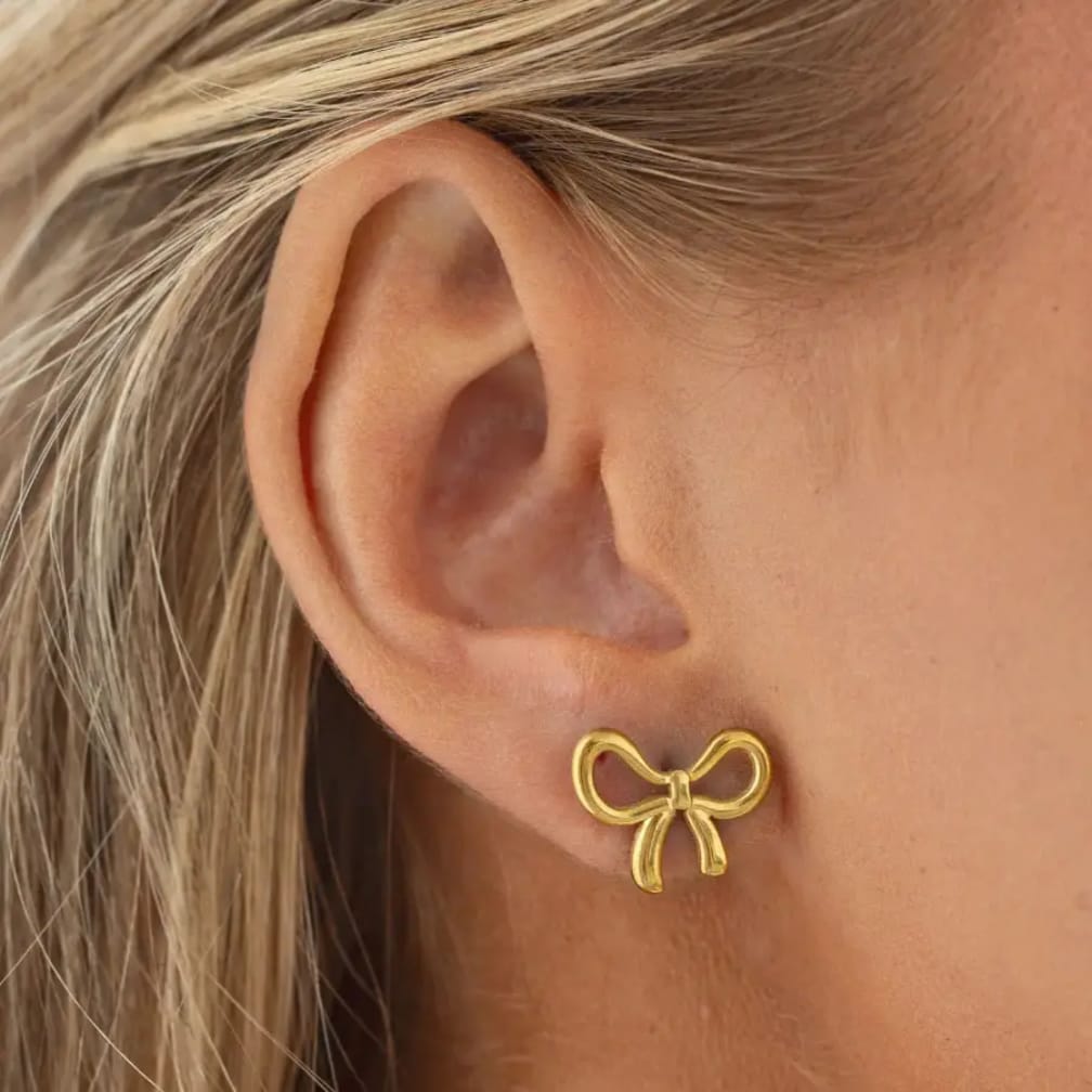 Gold bow stud earrings worn on ear – minimalist ribbon design