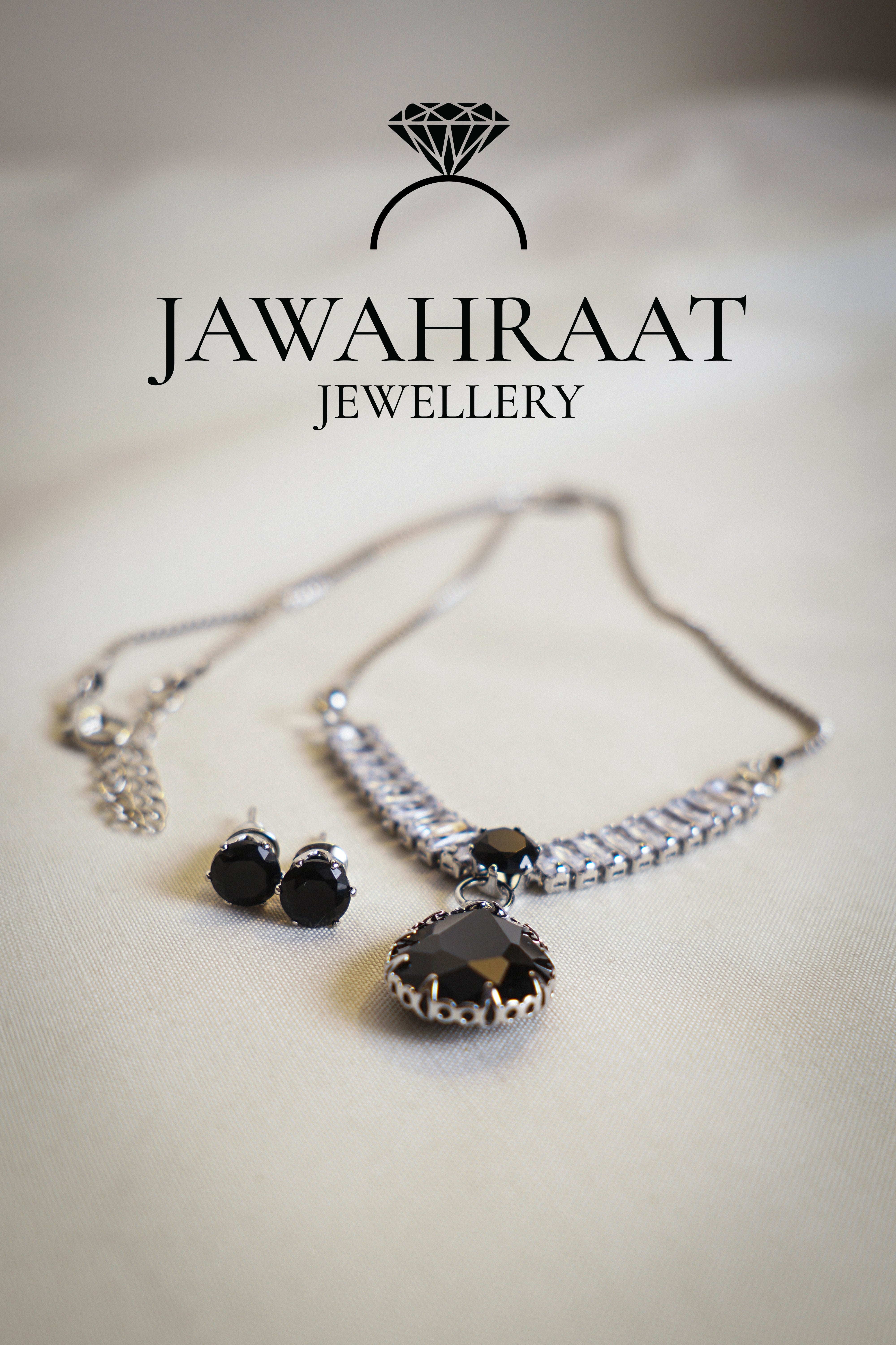 Elegant silver-toned necklace and earring set by Jawahraat Jewellery, featuring a black teardrop pendant and matching stud earrings, both adorned with sparkling crystal accents.

