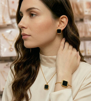Woman wearing black geometric gold plated fashion jewelry set with necklace bracelet and earrings