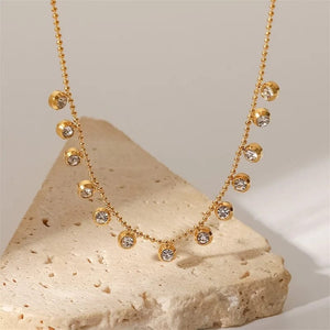 Gold beaded chain necklace with sparkling crystal drops on stone background