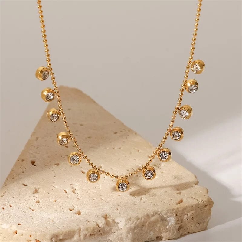 Gold beaded chain necklace with sparkling crystal drops on stone background