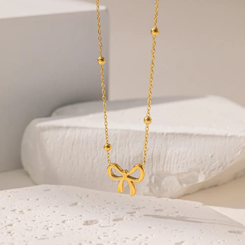 Gold bow pendant necklace with beaded chain on white background