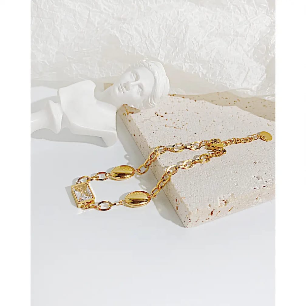 Gold bracelet with oval beads and crystal stone on textured background