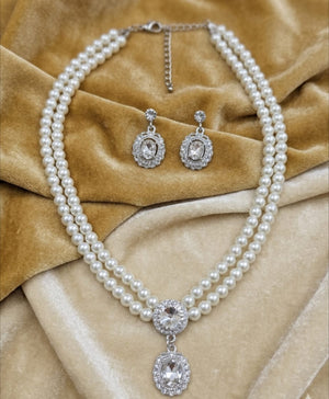Double strand pearl necklace with oval crystal pendant and matching drop earrings displayed on velvet background